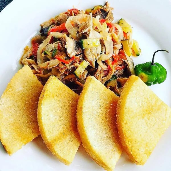 A plate of Jamaican ackee and saltfish with fried dumplings and a green scotch bonnet pepper.